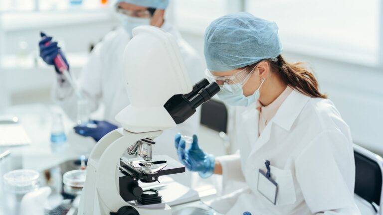 Researcher in protective gear examining a sample under a microscope in a laboratory_ illustrating SLU-PP-332 research and analysis